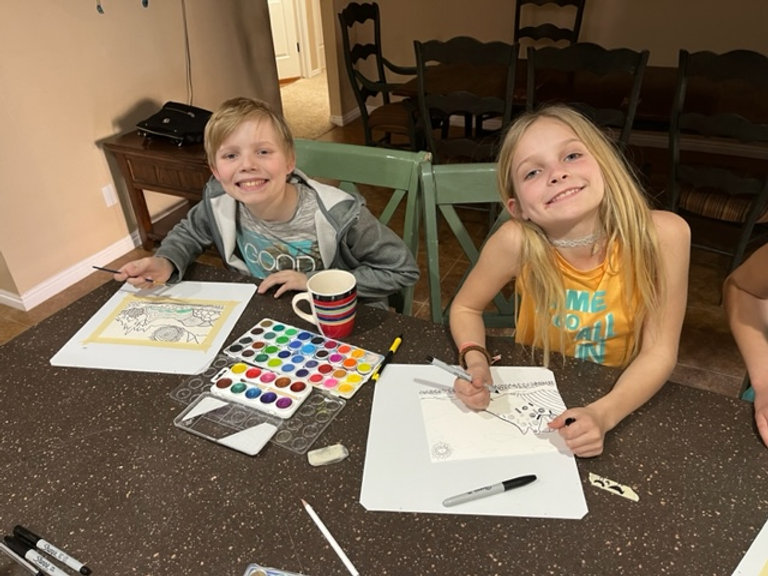 Three children sitting at a table, engrossed in painting and using markers to create colorful artwork.