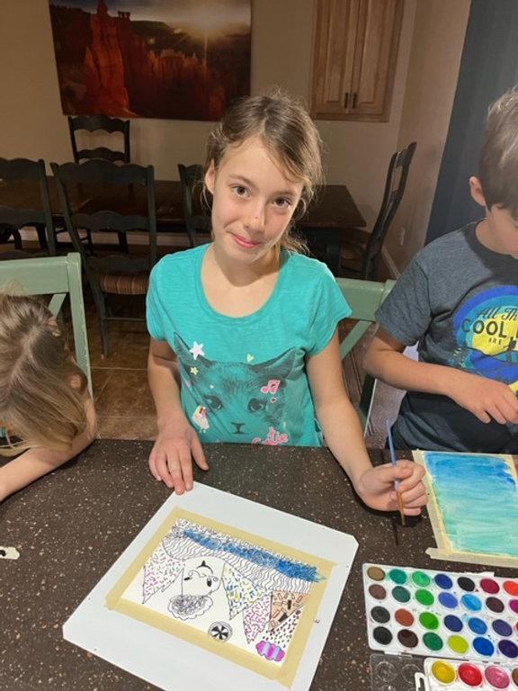 Three children sitting at a table, engrossed in painting and using markers to create colorful artwork.