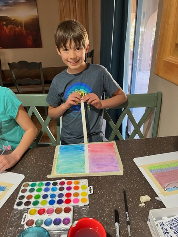 Three children sitting at a table, engrossed in painting and using markers to create colorful artwork.
