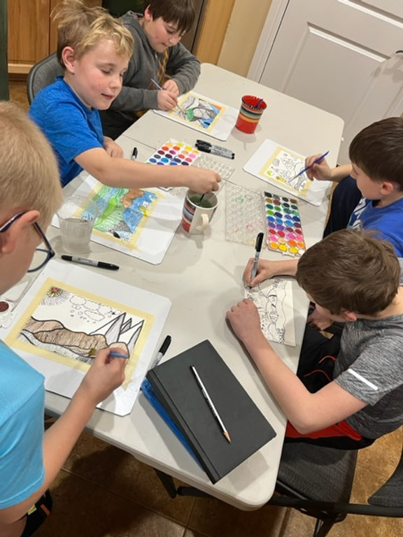 Three children sitting at a table, engrossed in painting and using markers to create colorful artwork.
